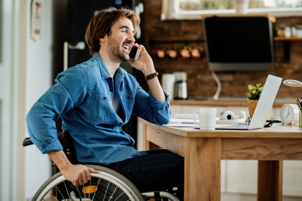 Young wheelchair user at his desk, on a phone call.