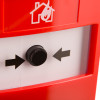 Closeup of the button on a manual call point showing black arrows pointing towards it on a red and white background