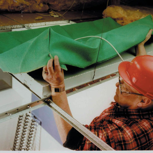 Man wearing a red hard hat and glasses fitting a green fabric in the Aflumican Astro Lumi Canopy Installation Above