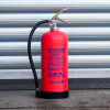 Red p50 6kg powder fire extinguisher standing in front of a metallic roller shutter door