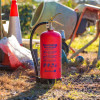 Red p50 6kg powder fire extinguisher standing on grassy ground near a work site mixer and traffic cones
