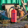 Red p50 6kg powder fire extinguisher standing on gravel with work site materials and a green container in the background