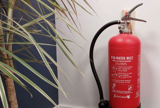 P50 6Ltr Water Mist Extinguisher hanging on wall next to a plant with a black hose and instructions visible