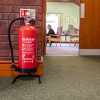 p50 6ltr water mist fire extinguisher on black stand against brick wall next to open doorway into room with chairs