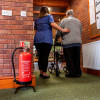 Red p50 6ltr water mist fire extinguisher on stand near a carer helping an elderly person through a door