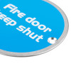 Closeup of a blue briton fire door keep shut sign with white text and a metal rim with a mounting hole