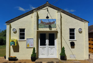 outside front of a church hall in a village with defibrillator and trees
