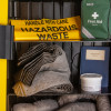 Closeup of open ultrafire yellow spill kit cabinet showing folded absorbent pads labelled hazardous waste and first aid kit