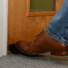 Foot wearing brown shoe pushing foot operated door opener decamed attached to wooden door base