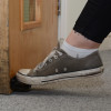 Foot wearing sneaker pressing foot operated door opener decamed fixed at bottom of wooden door panel