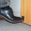 decamed stainless steel foot operated door opener fixed to wooden door being pressed by a foot in a black shoe