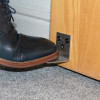 Close-up of a black boot pressing the stainless steel foot operated door opener decamed attached to the bottom of a wooden door