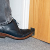 Foot wearing a dark shoe pressing the stainless steel foot operated door opener decamed attached to a wooden door base