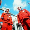 Two workers wearing protective clothing and hard hats with a drager 3200 fire escape mouth piece at work