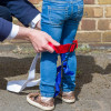 Child putting on a paraid child carrier harness with red and blue straps around their legs and waist