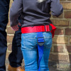 Child wearing paraid child carrier harness with red and blue straps fitted around waist and legs