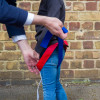 Adult securing paraid child carrier harness around child standing outside against a brick wall