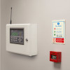 zerio plus 8 zone control panel installed on a wall at an angled view with a fire action notice and red fire alarm below