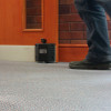 Close up low angle of dorgard fire door retainer fitted to the base of a wooden door with a person’s foot nearby