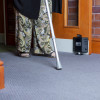 Person walking with a walking stick through an open door with dorgard fire door retainer visible on the door base