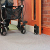 Close up of dorgard fire door retainer fitted to a door with a person using a walking aid nearby