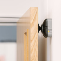 fireco dormag pro magnetic door holder attached to a wooden door holding it open against a white wall