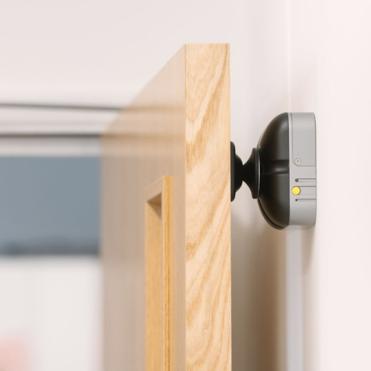 fireco dormag pro magnetic door holder attached to a wooden door holding it open against a white wall