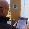 Person holding an Aurora iPad screen showing fire door inspection data next to a fire door keep shut sign