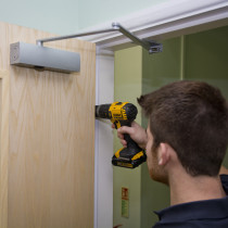 Close up of installer using drill to fit screws into hinges during fire door installation