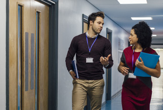 Two people walking past wooden fire doors for schools in a brightly lit school corridor