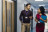 Two people walking past wooden fire doors for schools in a brightly lit school corridor