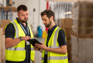 Two men wearing high-visibility vests conducting a Fire Extinguisher Site Survey in a warehouse environment