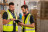 Two men wearing high-visibility vests conducting a Fire Extinguisher Site Survey in a warehouse environment