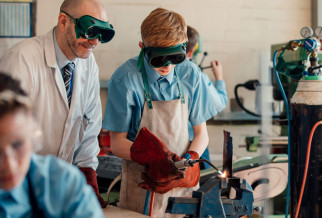 A teenage pupil using a welder under the supervision of a teacher