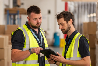 Two men wearing high-visibility vests looking at a tablet in a warehouse for Fire Risk Assessment Case Studies