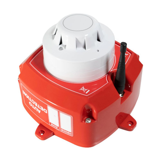 An angled view of a red fire safety unit featuring a white smoke detector on top and a black antenna on the side. The housing includes labelled zone indicators and a warning symbol printed on the surface.
