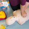Frtotaed First Response Training Aed and Cpr Course Manikin with hands performing chest compressions and AED pads being positioned