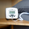 geofire agrippa deaf alart acoustic pillow alarm on wooden bedside table next to bed with grey pillow and white coiled cord