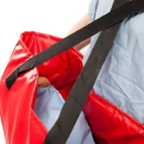 Close up of the red material and black straps of the buscot babevac evacuation cot with a small doll inside wrapped in blue fabric