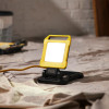 hispec 20w led work light with yellow frame switched on and placed on a cloth surface viewed from front in situ