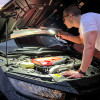 Person using hispec inspection torch to light inside engine compartment of a car with open bonnet in situ