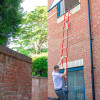 Man climbing down Hs2Stfel Hs3Stfel Ultrafire Fire Escape Ladder attached to first floor window of brick building