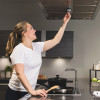 Person reaching up to adjust or clean a stainless steel kitchen range hood above a stovetop