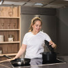 Person lifting the lid from a steaming pot on a modern induction hob, with a frying pan and utensils beside it