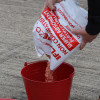 red metal fire bucket being filled with super absorbent granules from a white bag on a concrete surface