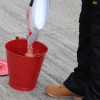 Red metal fire bucket being filled with granular material shown from above on a concrete surface