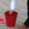 Red metal fire bucket on concrete floor with person pouring contents from a white bag into the bucket