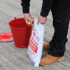 Red metal fire bucket on the ground next to a person holding a white refill bag with red text