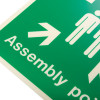 Close up of an assembly point sign rigid plastic showing white arrow and figures on a green background