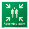 Front view of assembly point sign rigid plastic showing two white figures with arrows pointing inward on green background and assembly point text